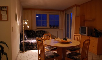 Offener Wohnraum mit Couch, Esstisch und Zugängen zum Kochbereich und zum Balkon